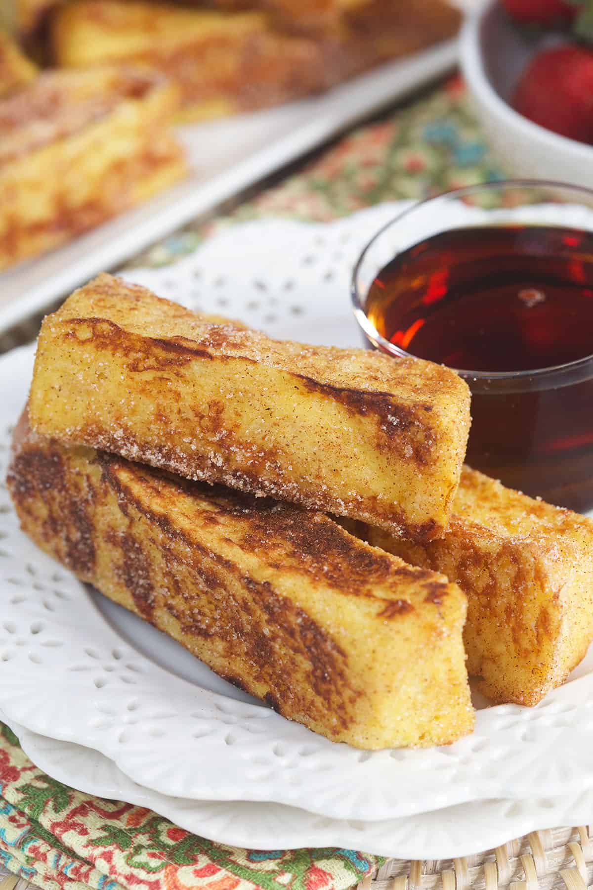 A white plate is topped with french toast sticks and syrup.