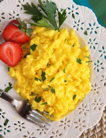 Scrambled eggs are placed on a white plate with sliced srawberries.