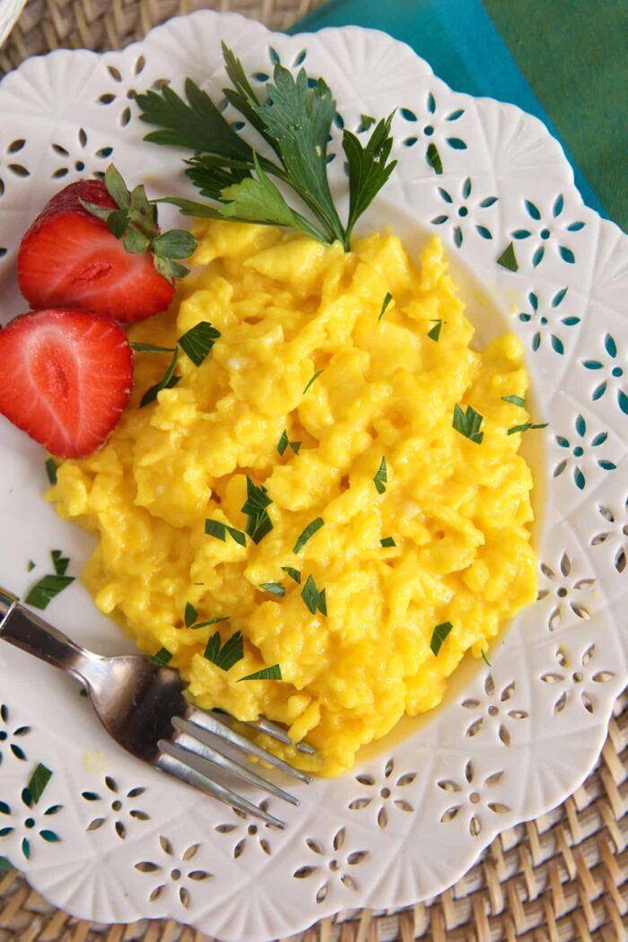 Scrambled eggs are placed on a white plate with sliced srawberries.