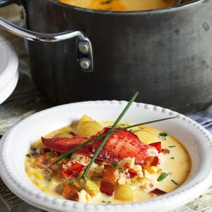 Lobster Corn Chowder in a white bowl with a black pot in the background.