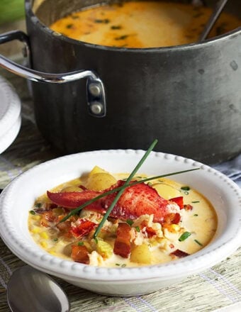 Lobster Corn Chowder in a white bowl with a black pot in the background.