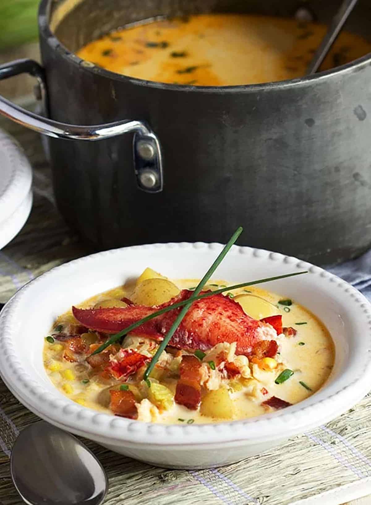 Lobster Corn Chowder in a white bowl with a black pot in the background.