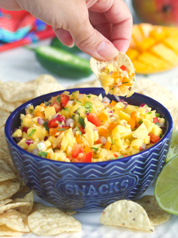A chip is scooping up some mango salsa out of a blue serving bowl.