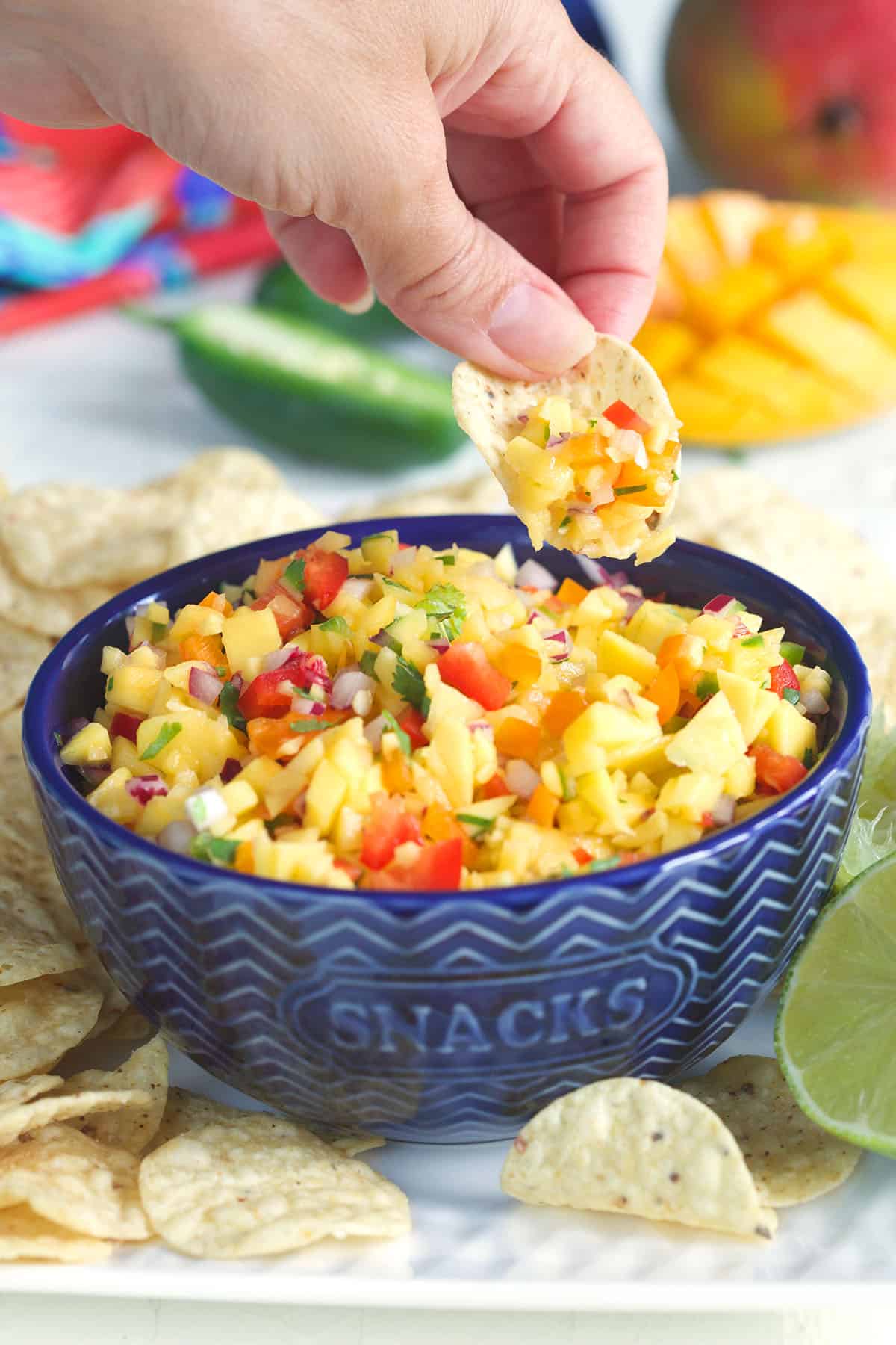 A chip is scooping up some mango salsa out of a blue serving bowl.