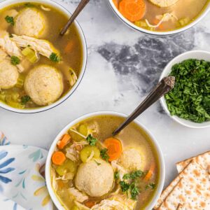 Three bowls of matzo ball soup are placed on a marble countertop.