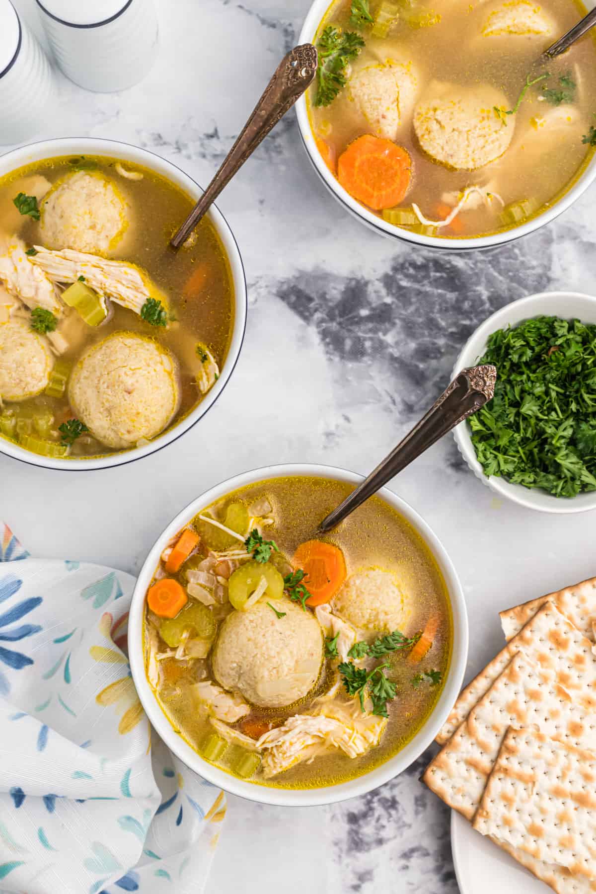 Three bowls of matzo ball soup are placed on a marble countertop. 