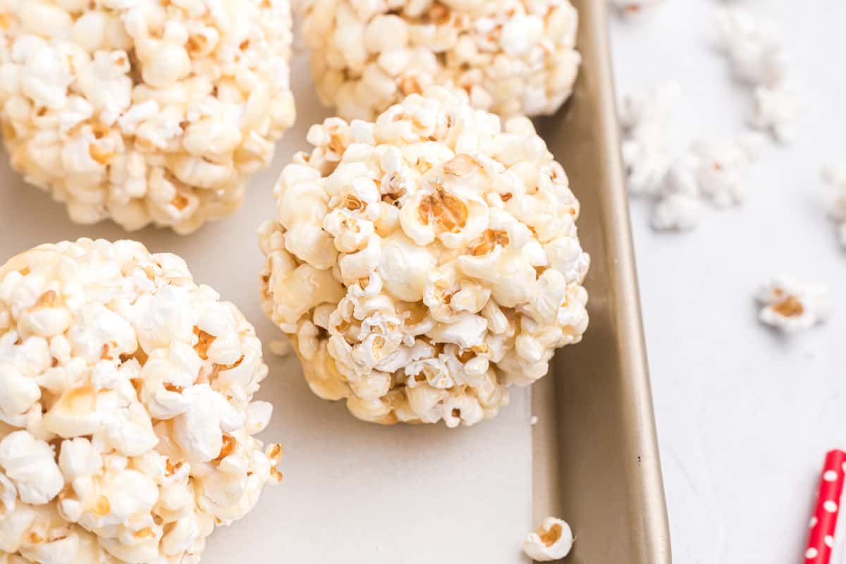 Several popcorn balls are placed on a baking sheet covered in parchment paper.