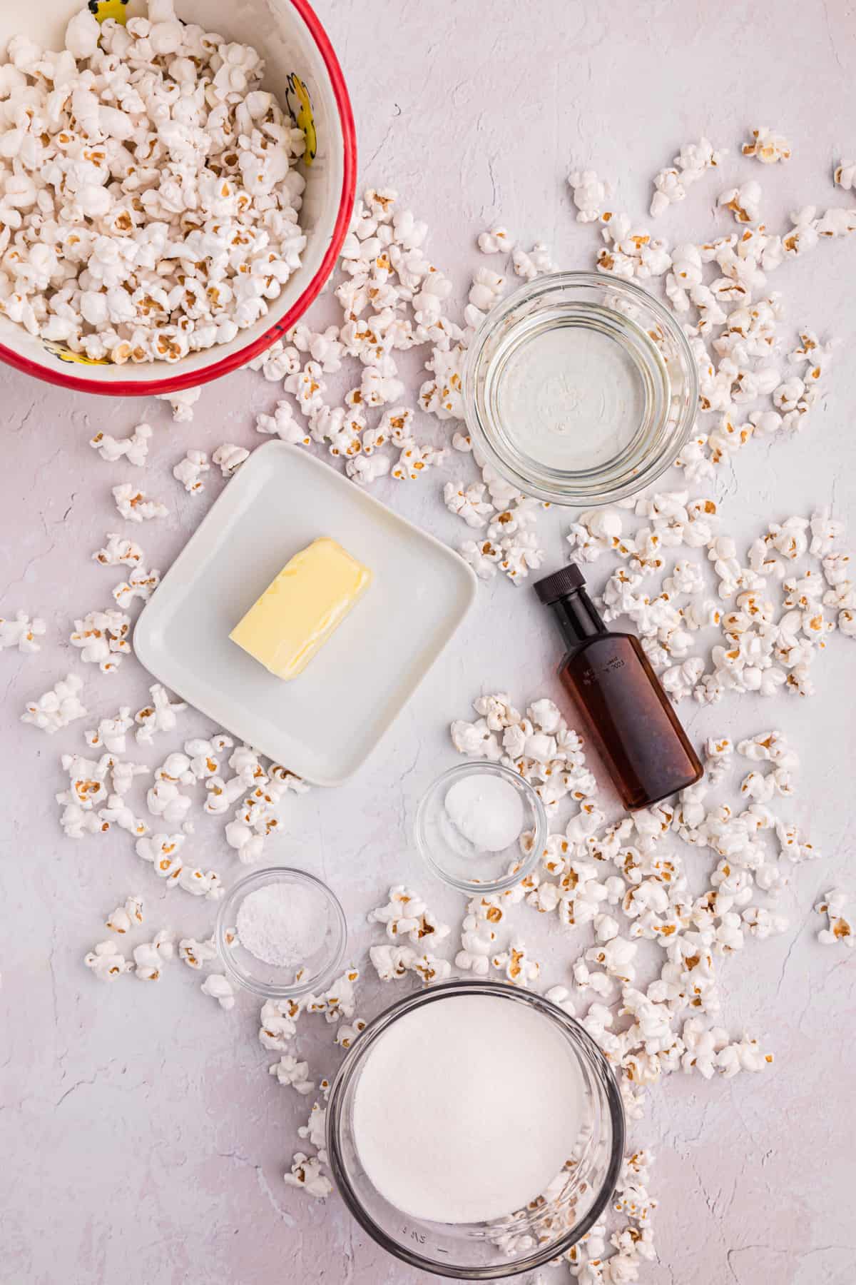 Popcorn is spread around several other ingredients on a white surface.