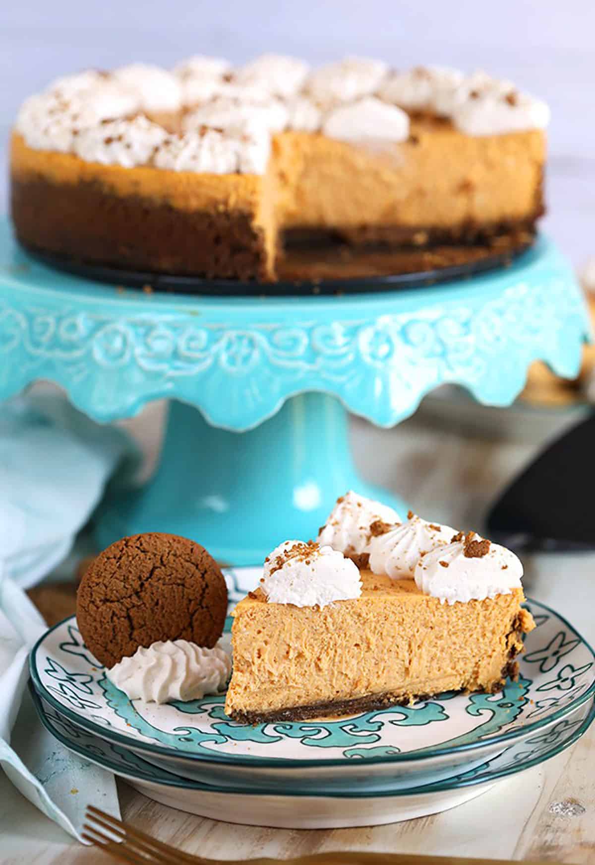 Pumpkin Cheesecake on an turquoise cake plate with a slice of cheesecake on a plate in front of it.