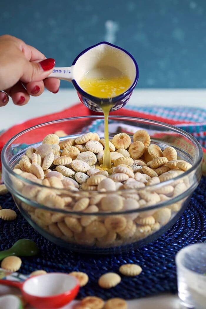 butter being poured over oyster crackers in a glass bowl.