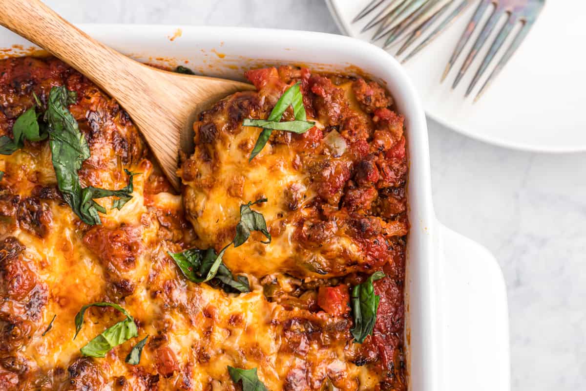 A wooden spoon is lifting a portion of lasagna from the baking dish.