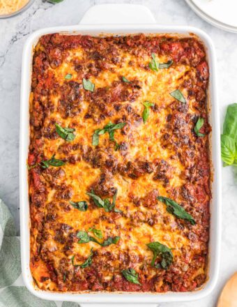 A white baking dish is filled with baked ravioli lasagna.