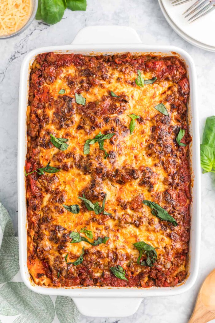 A white baking dish is filled with baked ravioli lasagna.