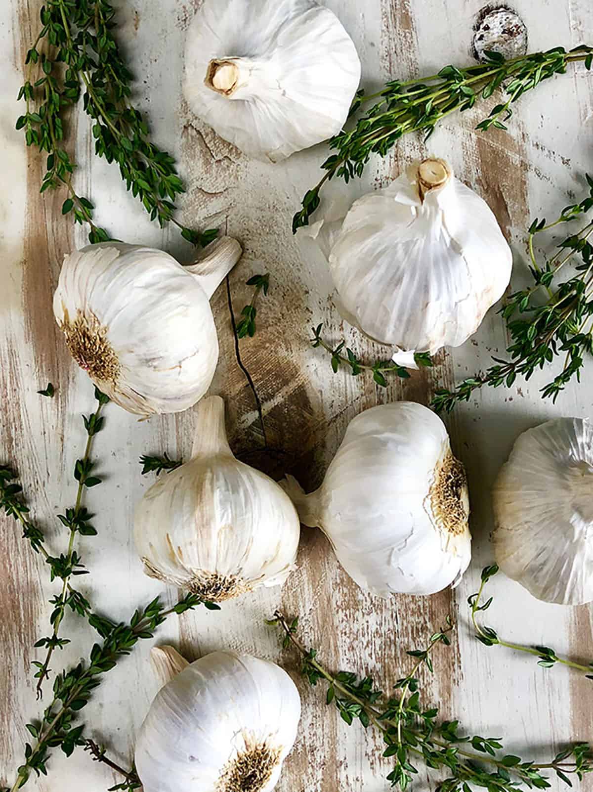 Garlic bulbs and thyme on a whitewashed cutting board. 