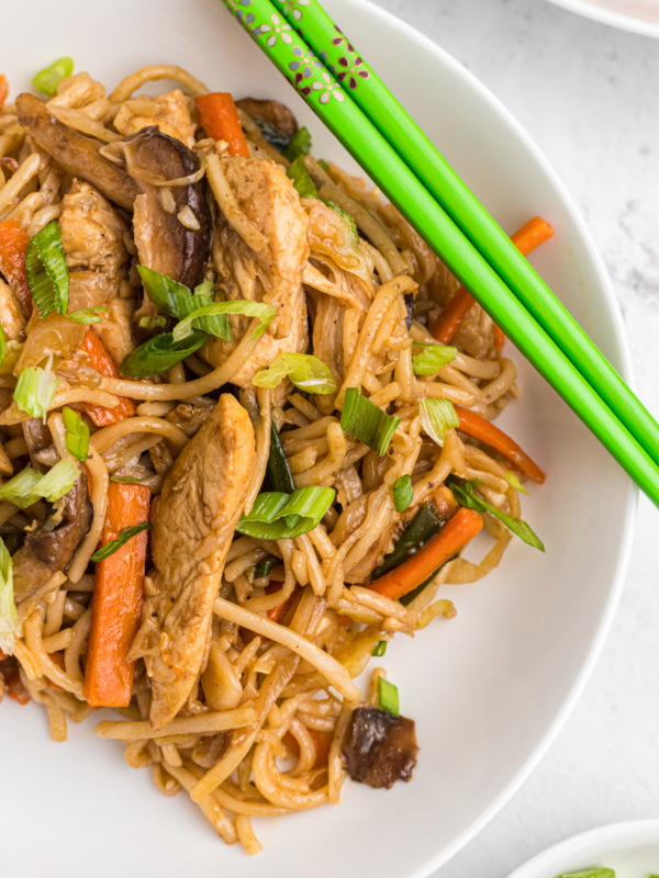 Green chopsticks are placed on a white bowl with a serving of yakisoba.