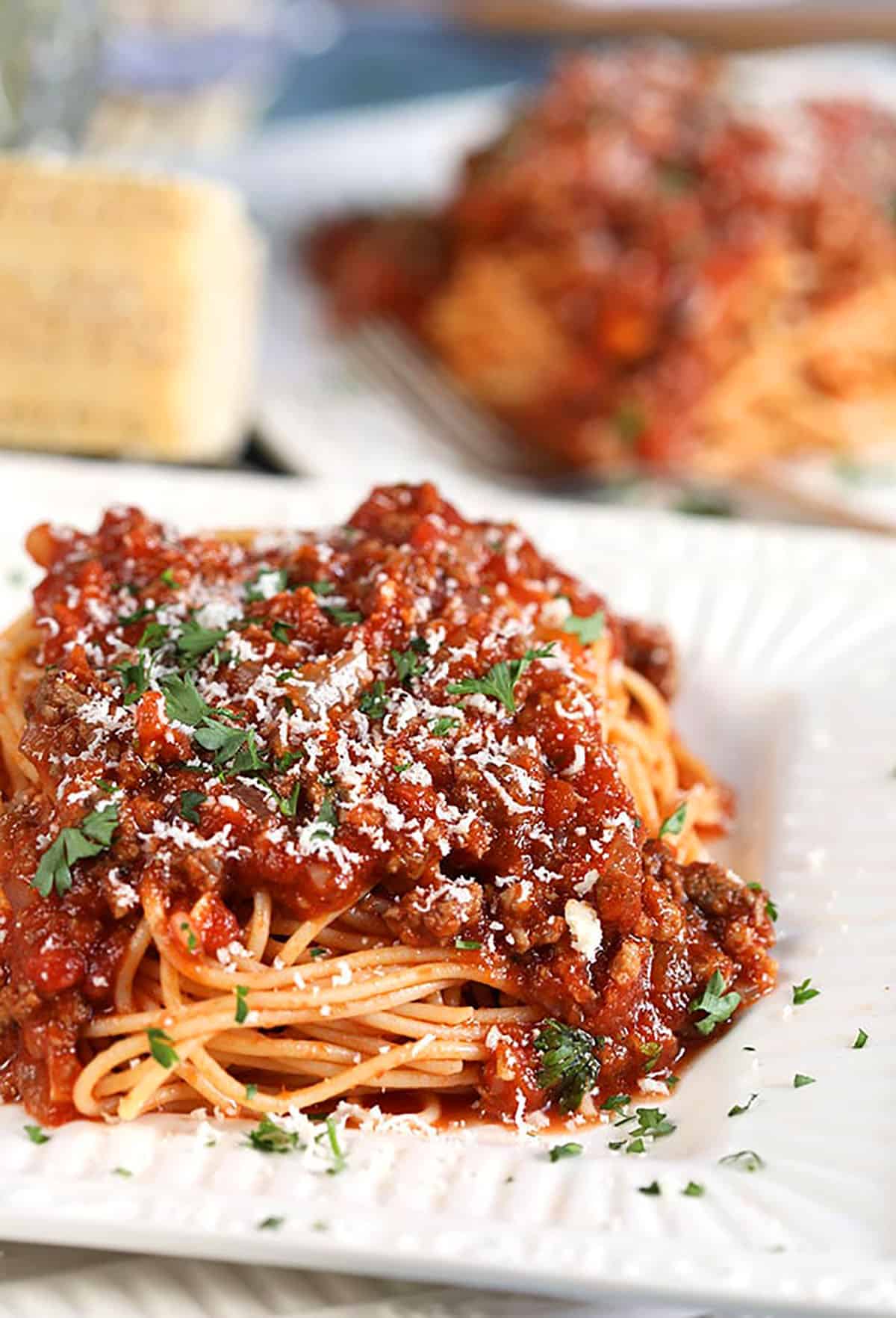 Spaghetti with Easy Italian Meat Sauce on a white square plate and wedge of cheese