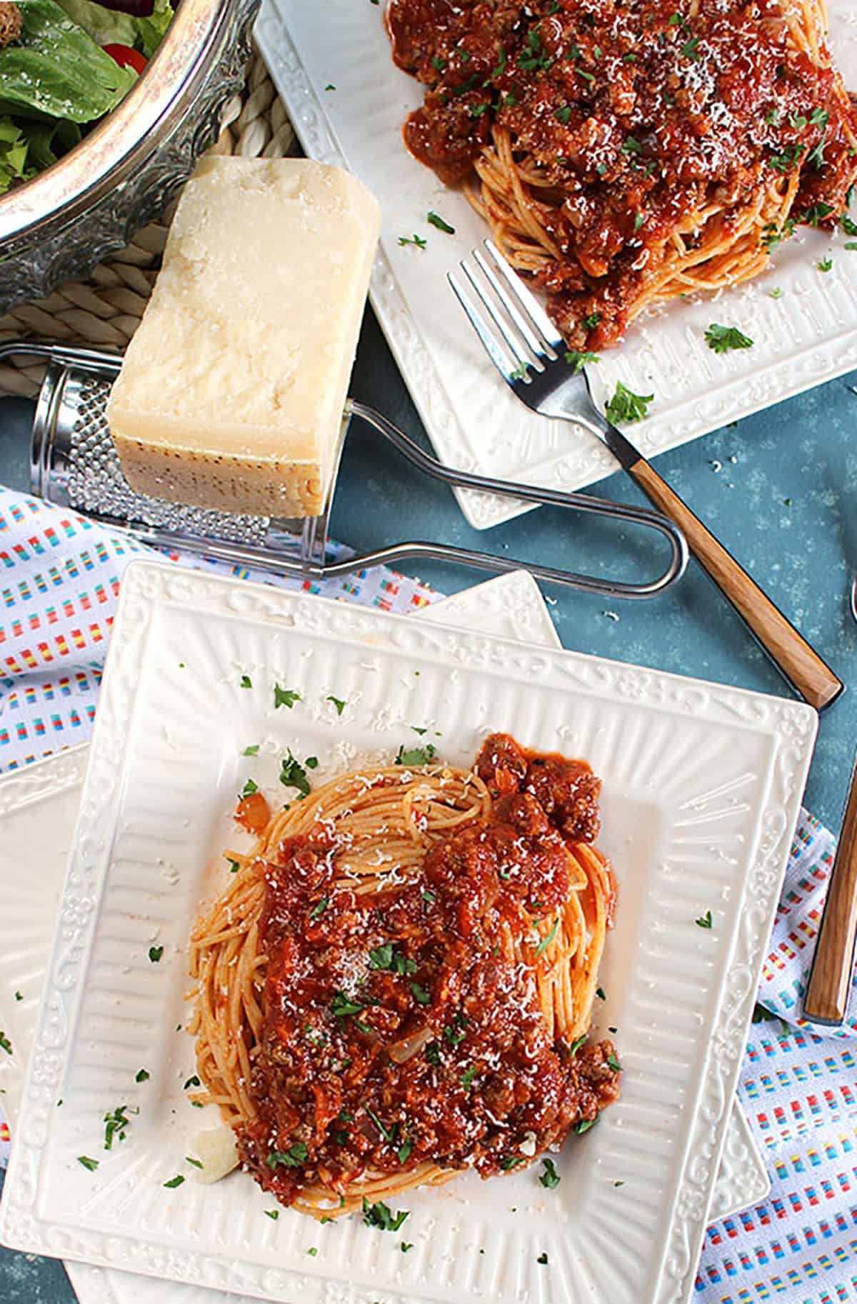 Spaghetti and Easy Italian Meat Sauce on a square plate with a bowl of salad on a blue background