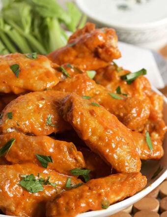 Buffalo wings in a white serving bowl with celery in the background.