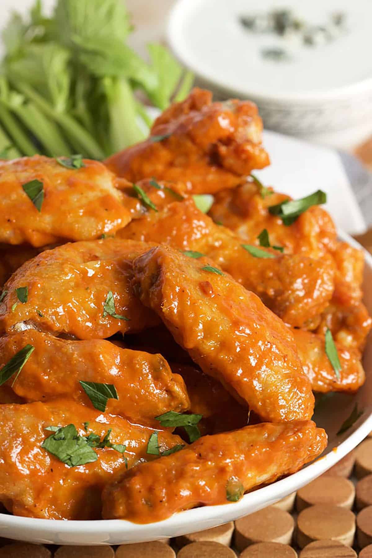 Buffalo wings in a white serving bowl with celery in the background.