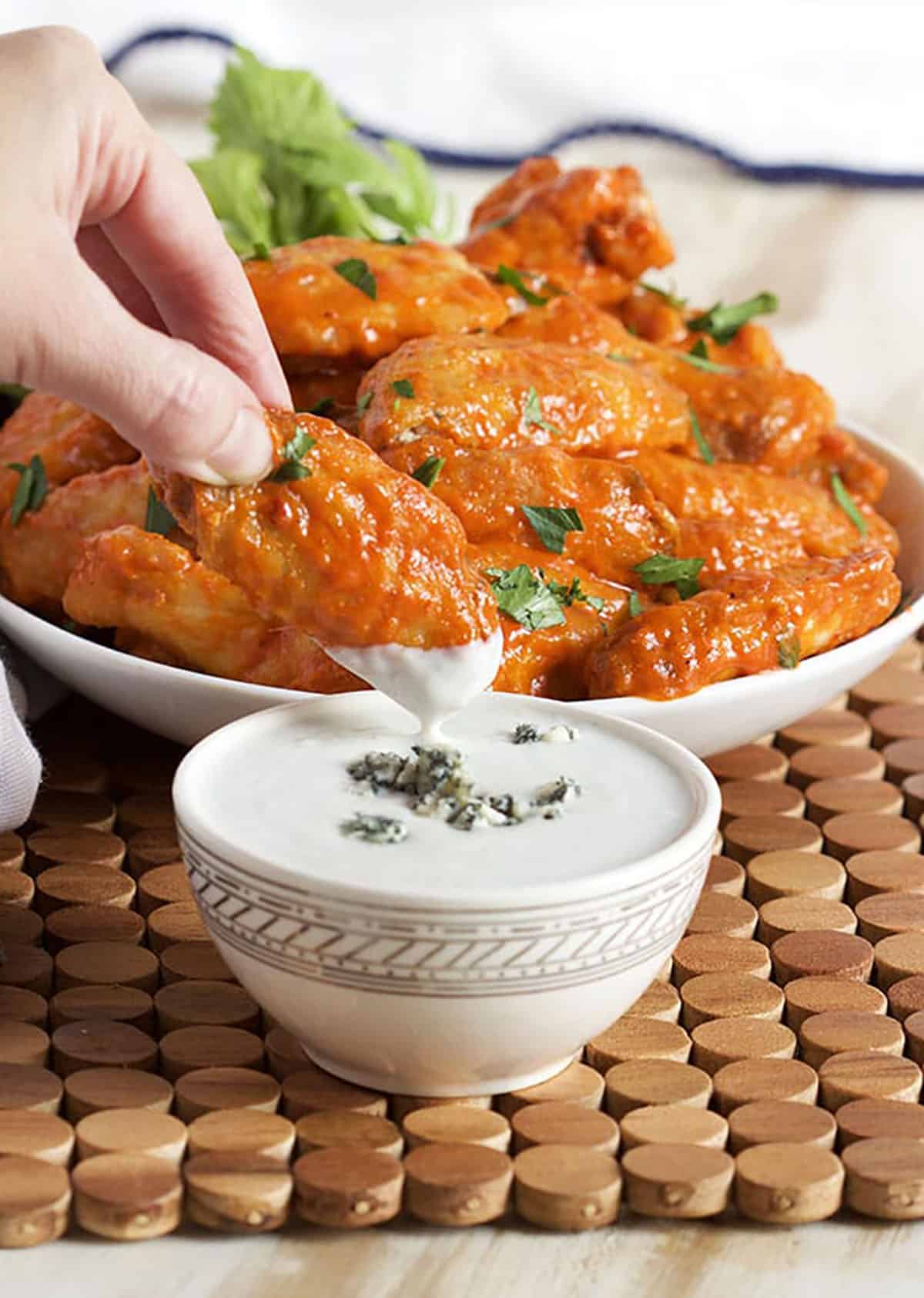 Buffalo chicken wing being dipped into a white bowl of blue cheese dressing.