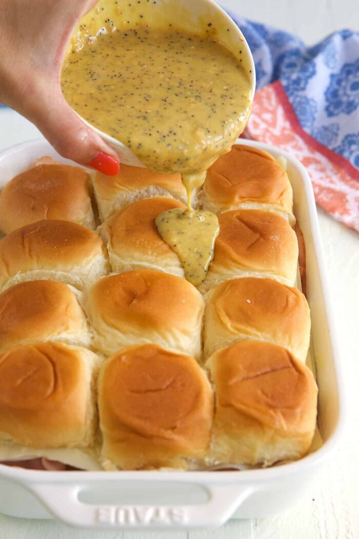The mustard sauce is being drizzled on top of the sliders.