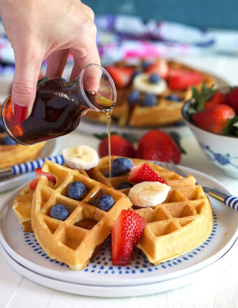 Belgian Waffle with fruit and syrup being poured over top.