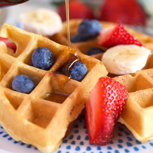 Belgian waffle on a white plate with fruit.