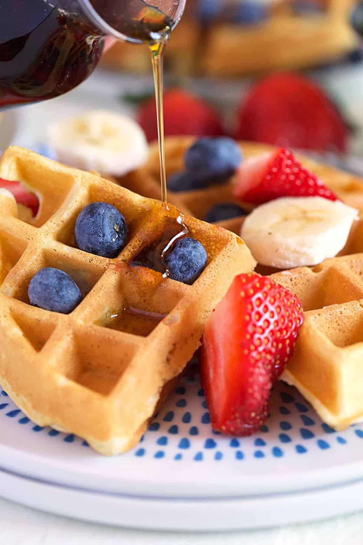 Belgian waffle on a white plate with fruit.
