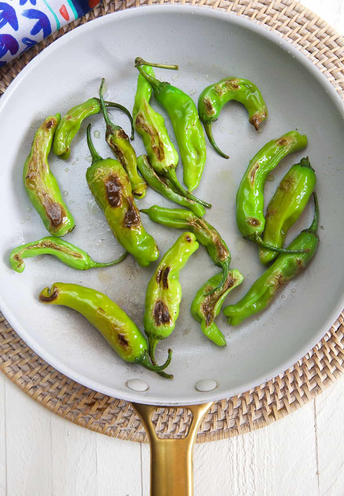 Several blistered shishito peppers are in a skillet.