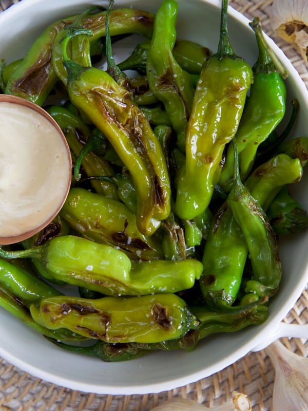 A bowl filled with blistered peppers is placed on a table.