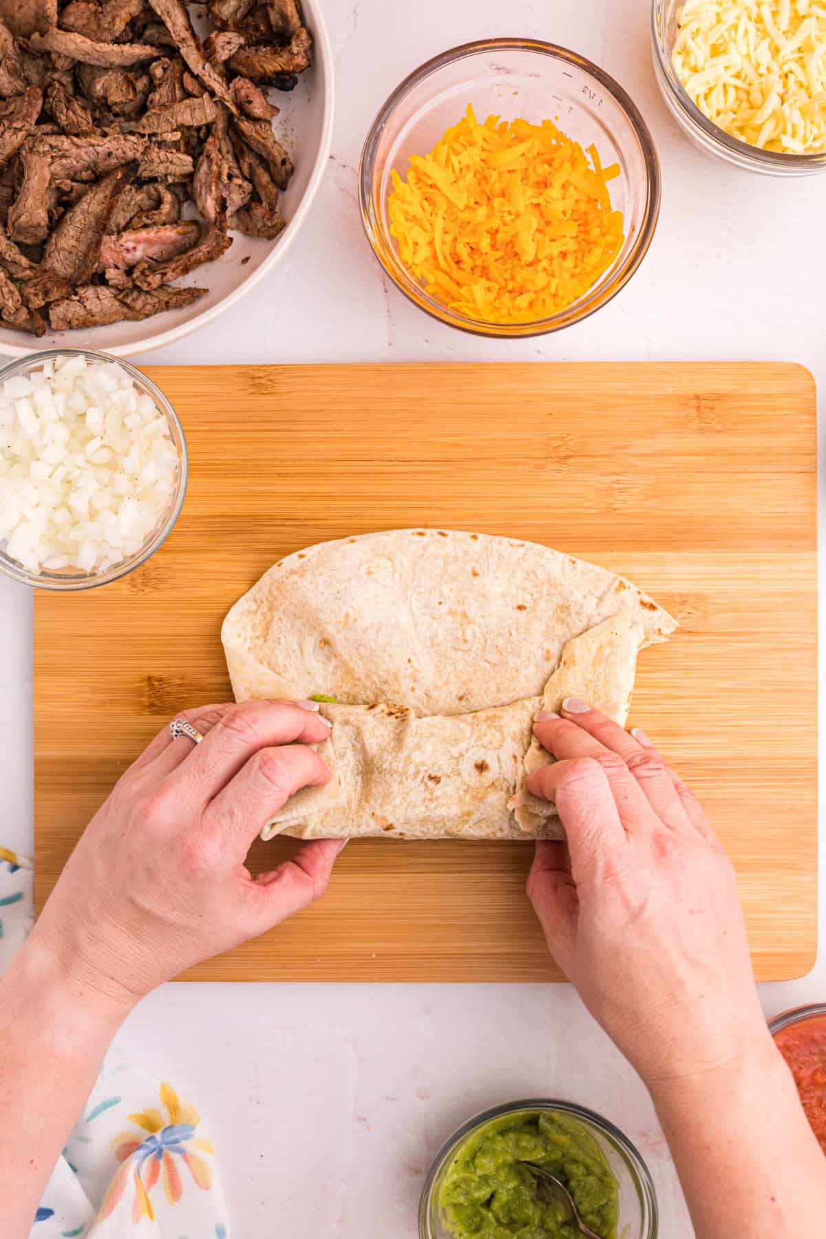 A burrito is being rolled on a wooden cutting board.