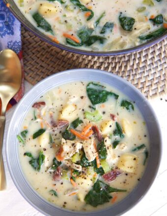 A bowl of chicken and gnocchi soup is placed next to a pot.