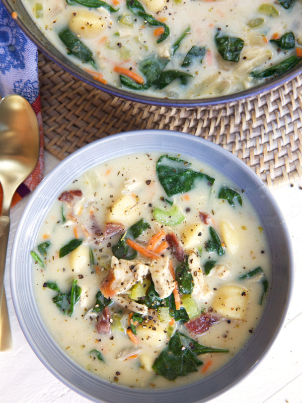 A bowl of chicken and gnocchi soup is placed next to a pot.