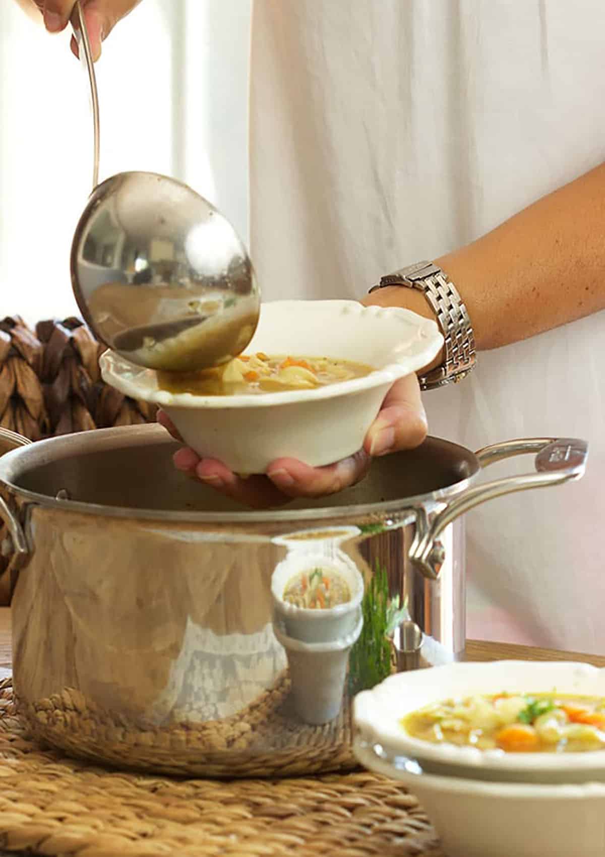 Chicken Noodle Soup being served from a stock pot with a ladle into a white bowl.