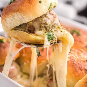 Meatball slider being served from a baking dish with cheese pulling down to the dish.