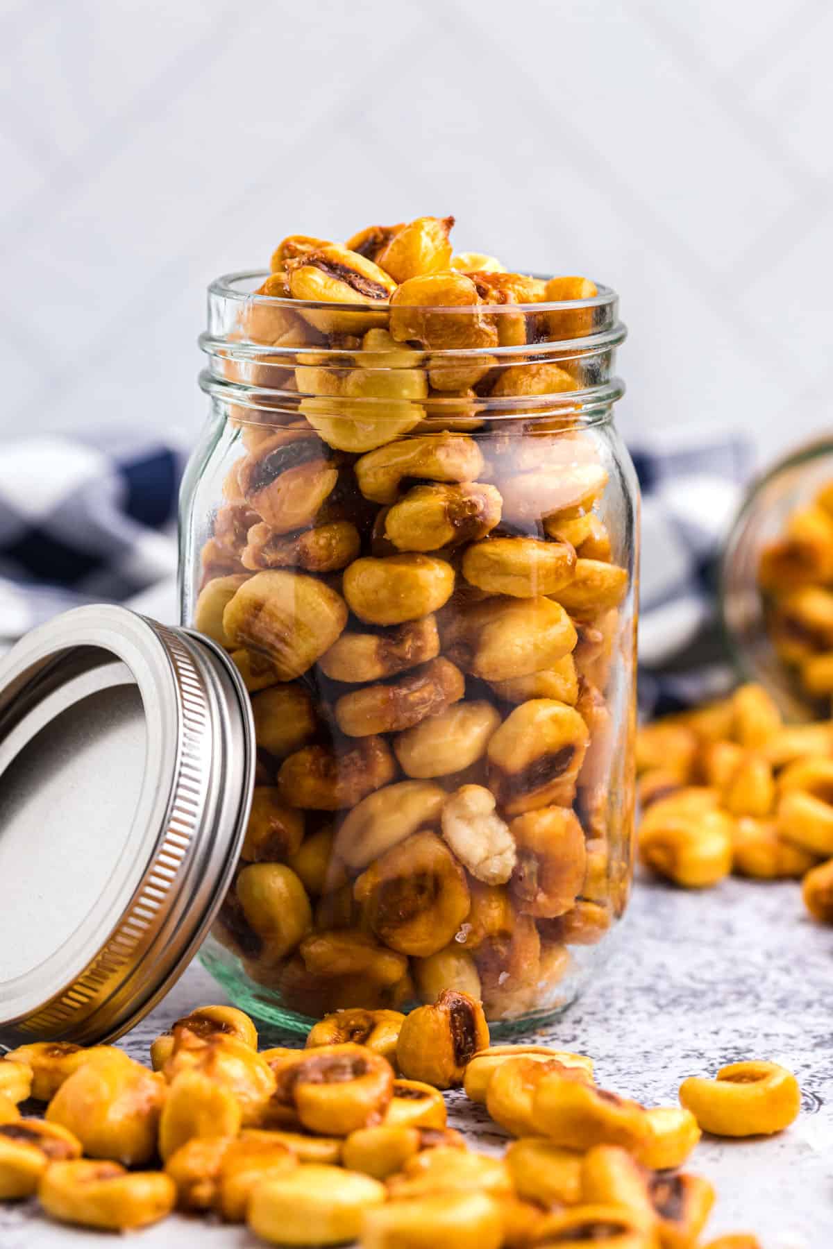 Seasoned corn nuts in a glass jar with a steel lid propped against the side of the jar.