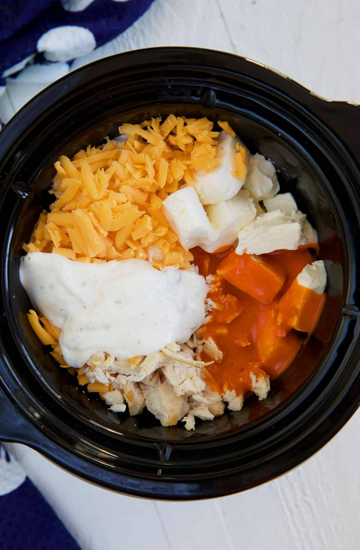 A Crockpot is filled with the ingredients for buffalo chicken dip.