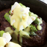 Steak Oscar in a skillet topped with asparagus and crab meat with hollandaise sauce.