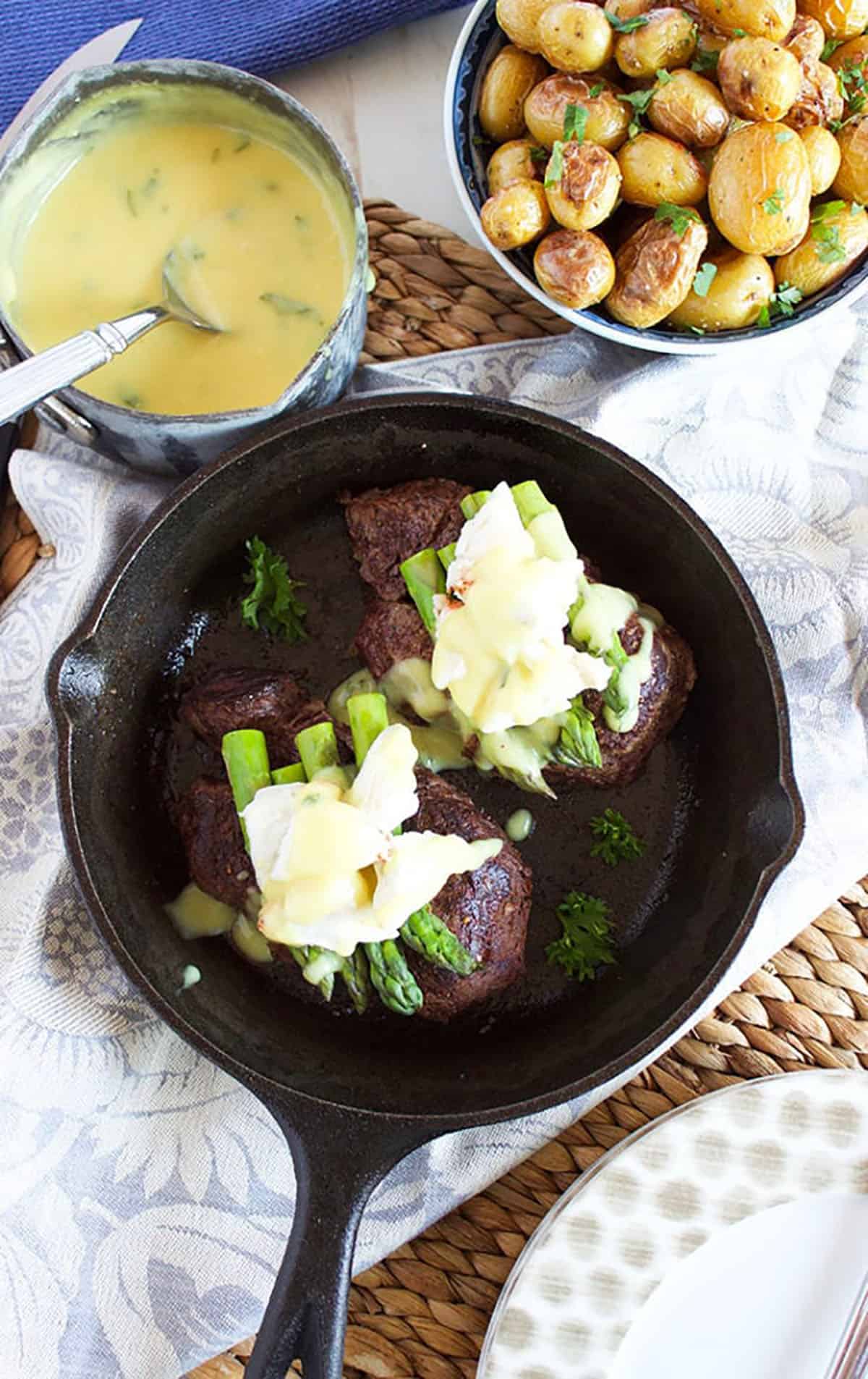 Filet Oscar in a cast iron skillet with a pan filled with béarnaise in it.