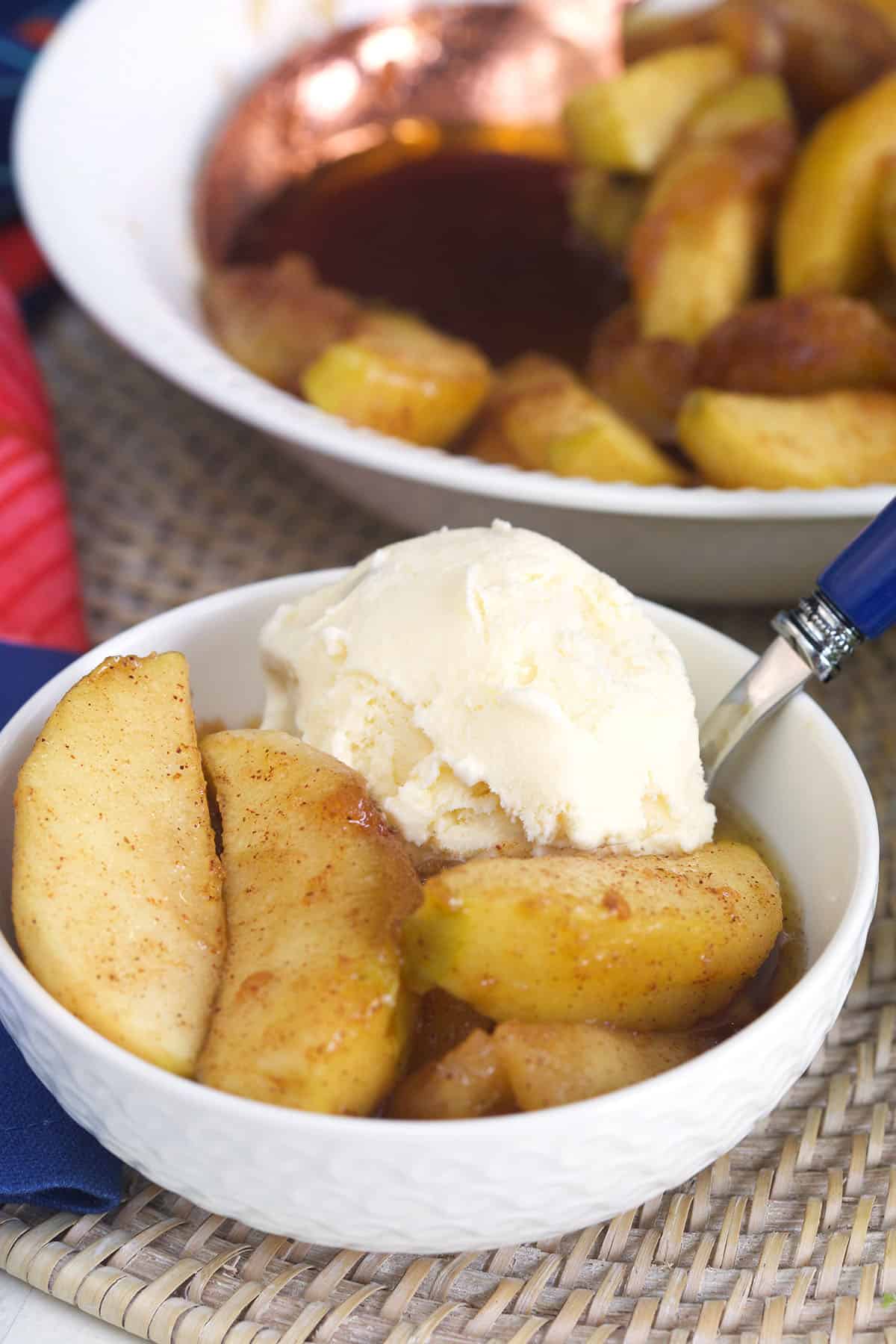 A scoop of ice cream is placed on top of fried apples in a bowl.