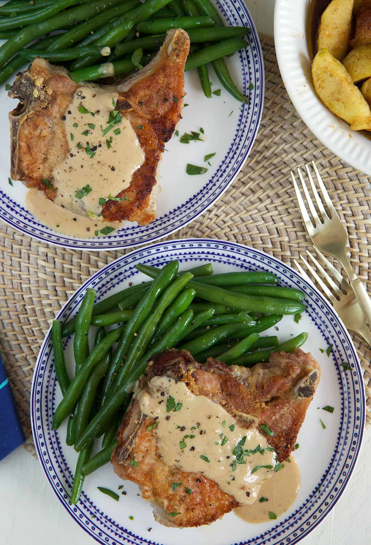 Gravy covered pork chops are placed next to green beans on a plate.
