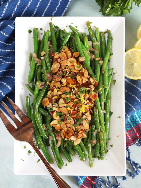 Overhead shot of green beans almondine on a white platter.