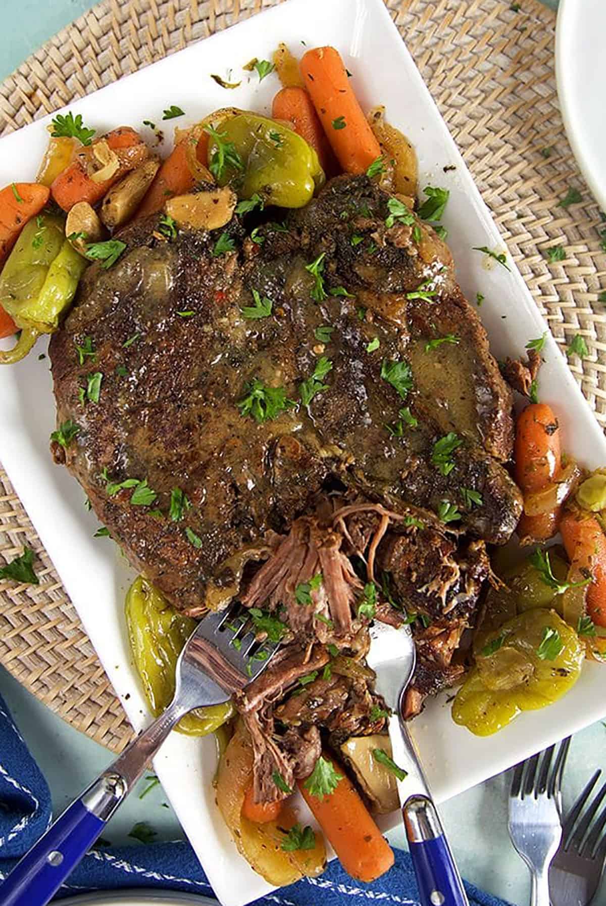Tender mississippi pot roast on a white platter with peppers, onions and carrots.