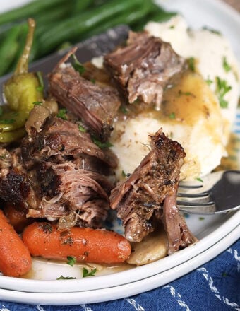 Mississippi Pot Roast on a pile of mashed potatoes on a white plate with green beans.