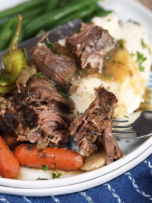 Mississippi Pot Roast on a pile of mashed potatoes on a white plate with green beans.