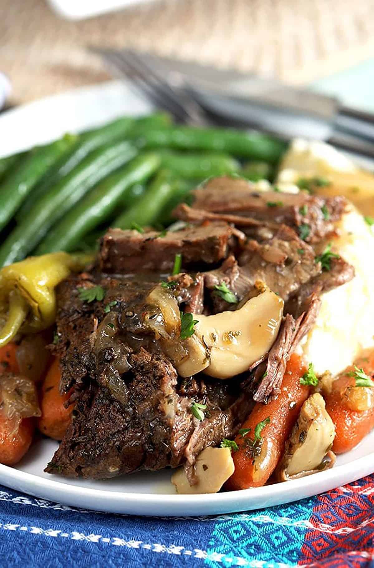 Mississippi Pot Roast slice with garlic on a bed of mashed potatoes with green beans in the background.