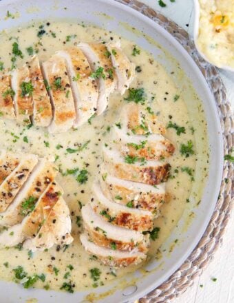Several sliced chicken breasts are coated in white sauce in a skillet.