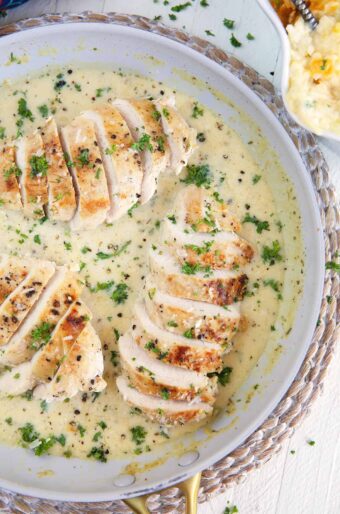 Several sliced chicken breasts are coated in white sauce in a skillet.