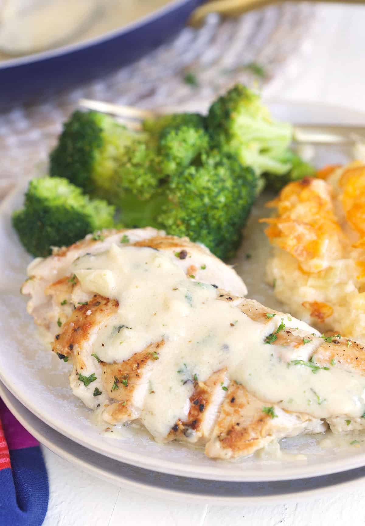 Broccoli and potatoes are placed next to a sauce covered chicken breast on a plate.