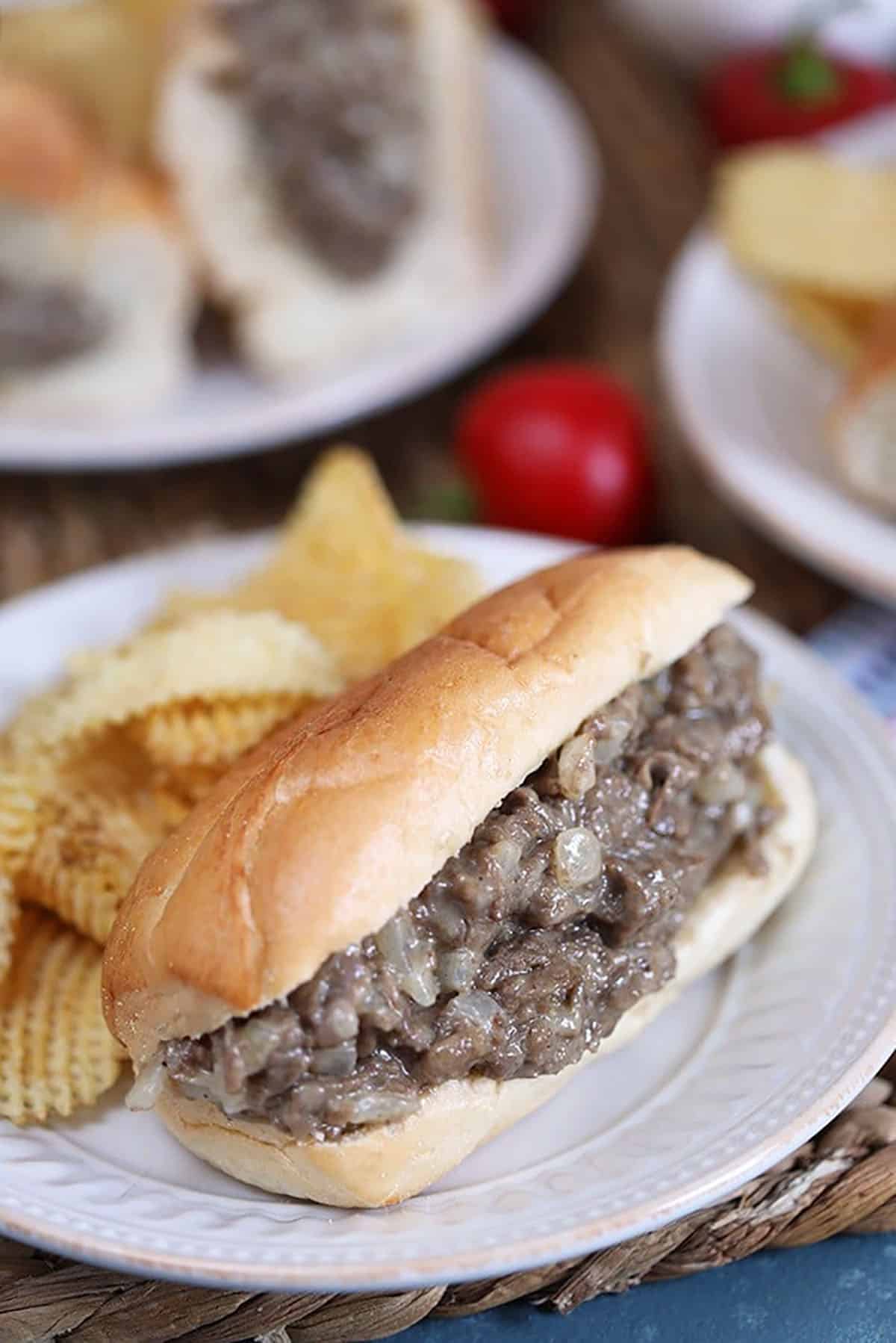Philly cheesesteak sandwich on a white plate with chips.